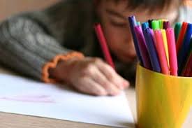Un alunno colora su un foglio di carta, in primo piano un bicchiere pieno di pennarelli.